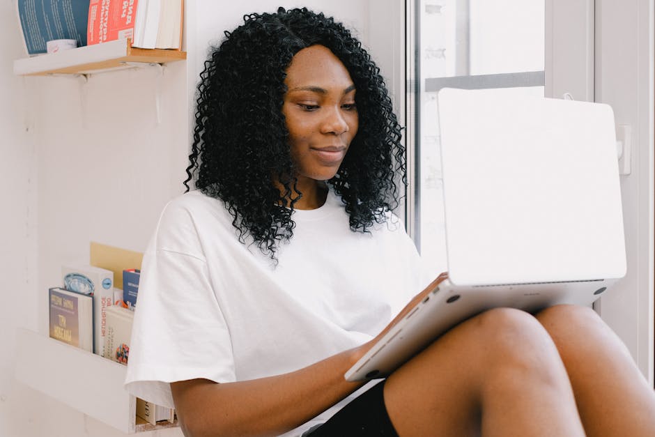 Positive African American female with curly hair freelancing on white netbook on knees in daylight